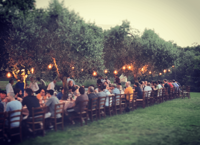 Outdoor dinner party with string lights and long communal tables in orchard
